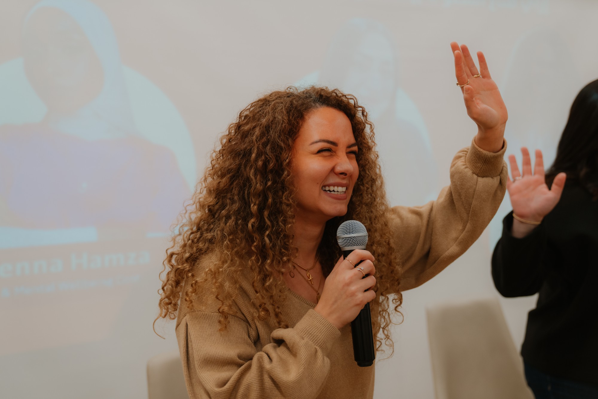 Nourhan Maher laughing and waving while speaking on stage with a microphone